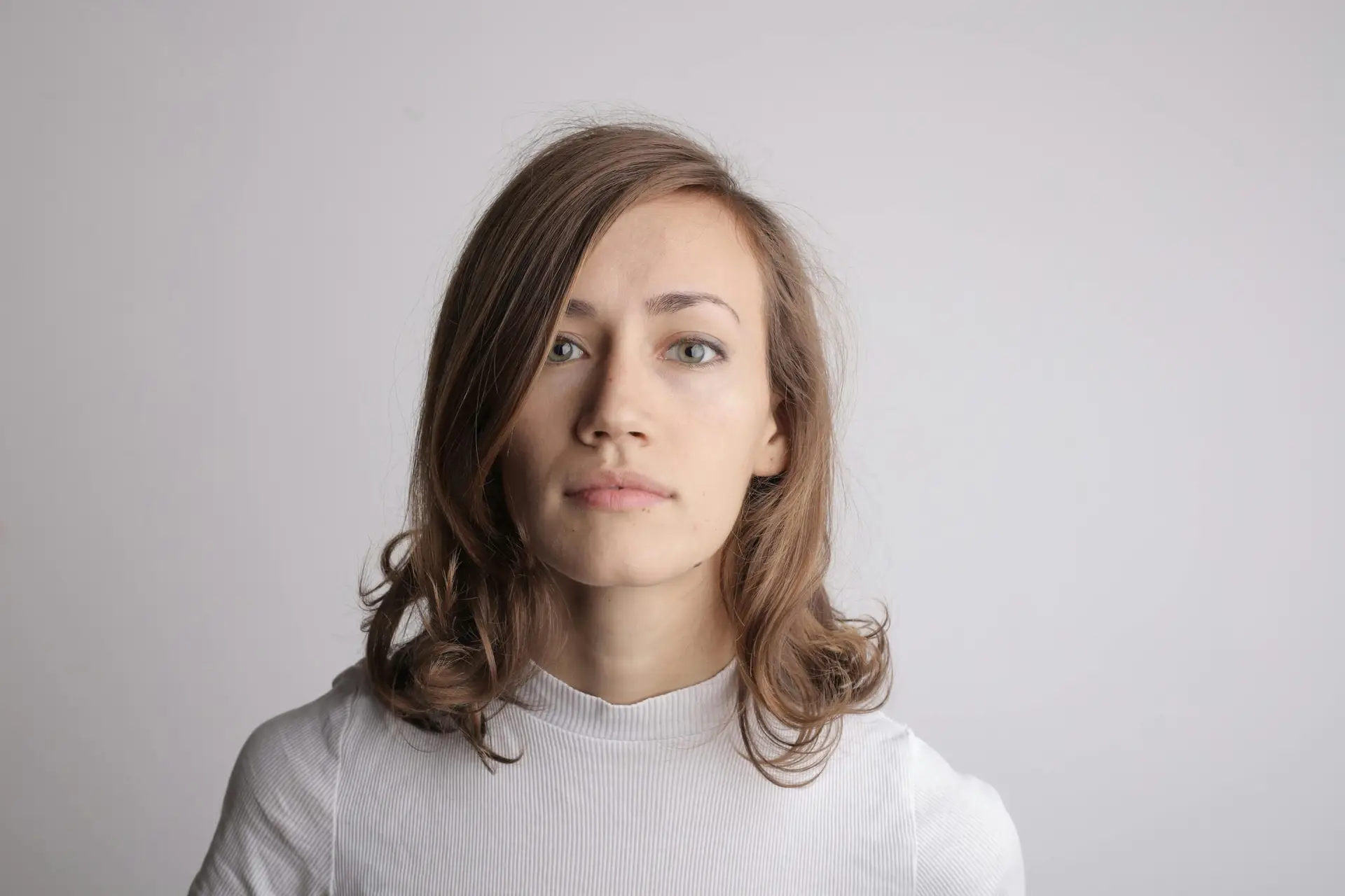 A serene portrait of a woman with brunette hair in a white turtleneck against a white background.