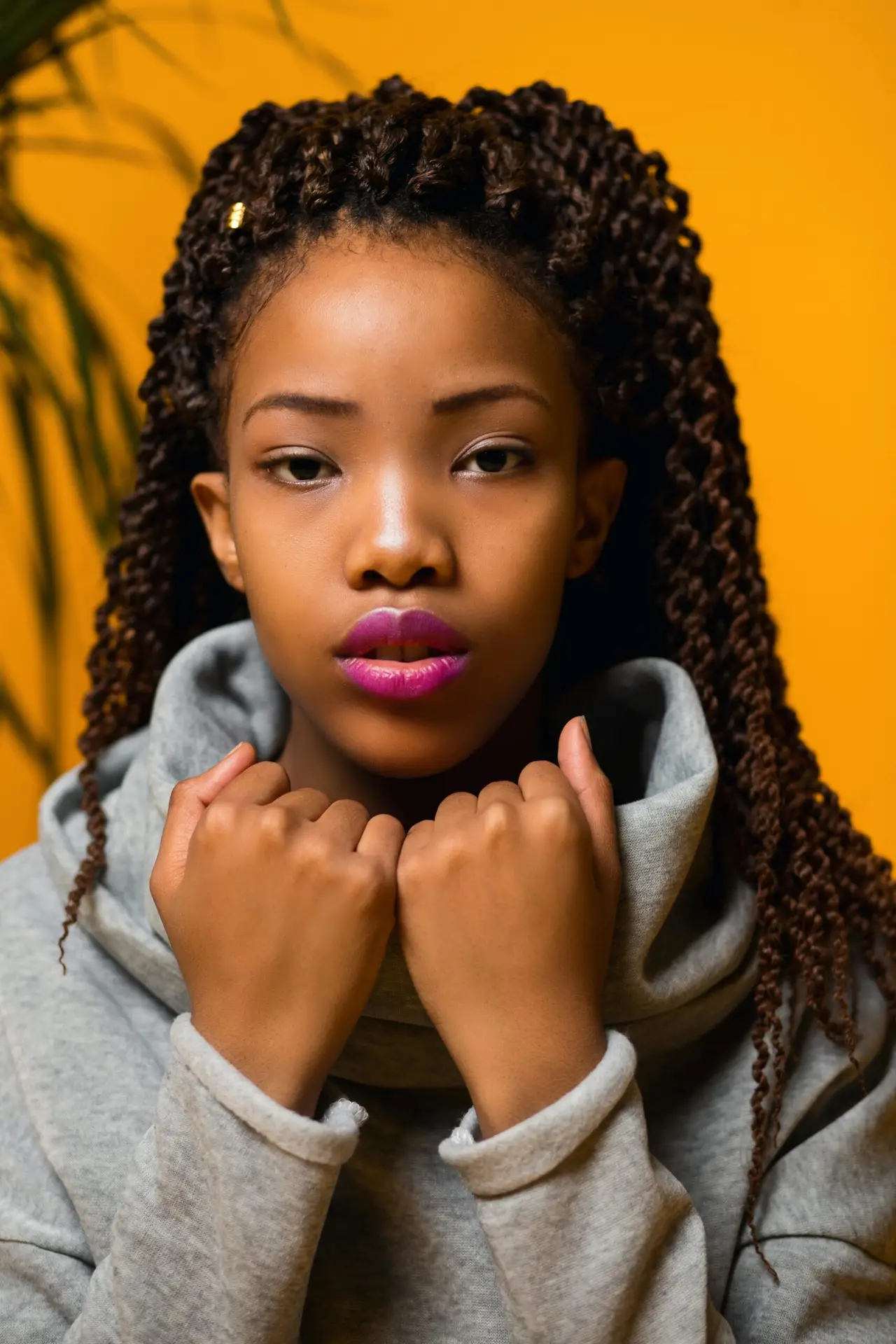 Striking portrait of a young woman with braids against a vibrant yellow backdrop.